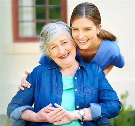 A smiling carer with her arms around an elderly woman
