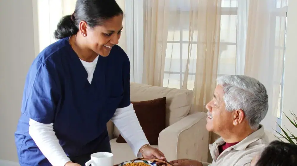 A carer bringing tea to an elderly man